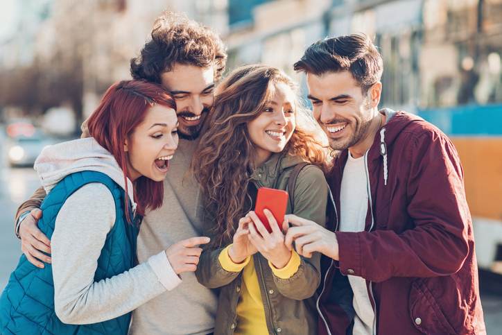 Group of young people watching at a smart phone and laughing Group of young people watching at a smart phone and laughing